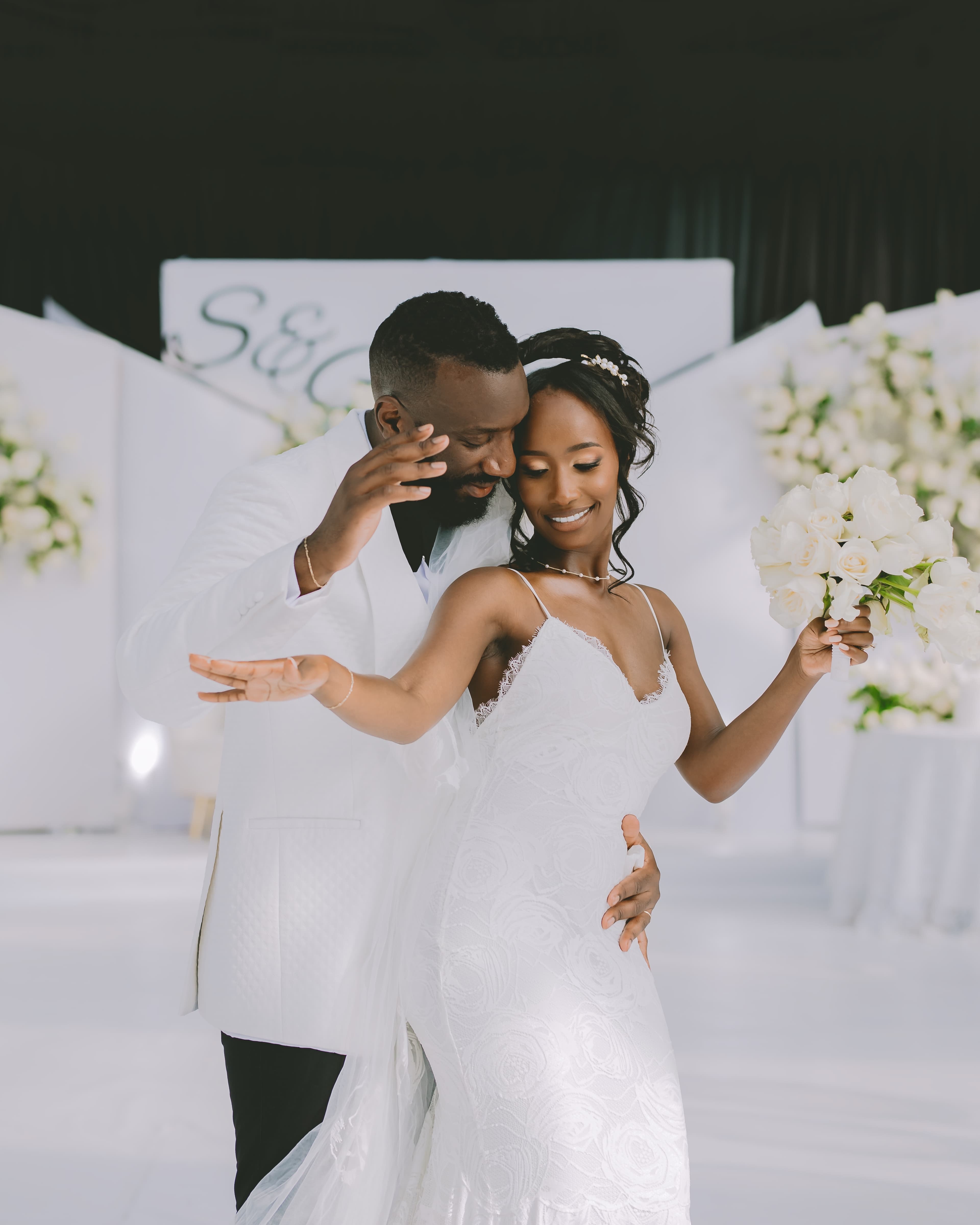 Joyful Black bride and groom dancing in white wedding attire at their elegant reception.