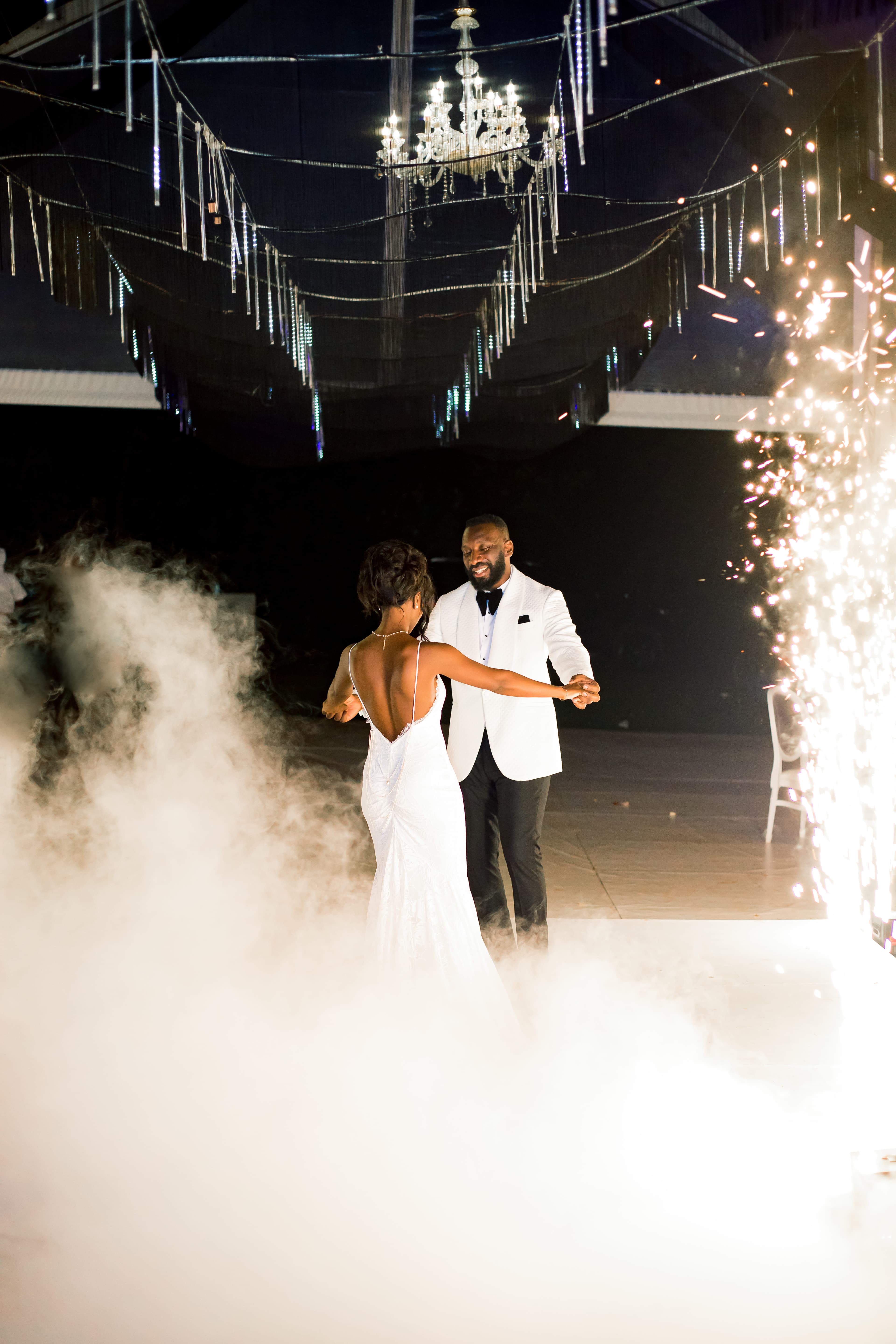 Newlyweds dance on a fog-filled floor surrounded by indoor sparklers and a crystal chandelier.